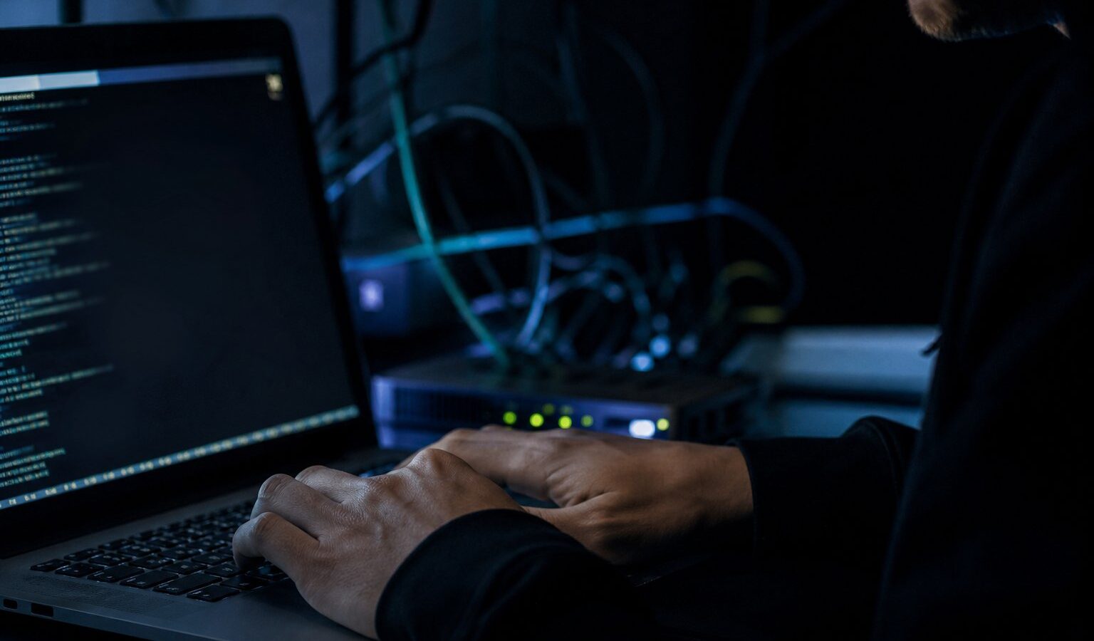Hands typing on a laptop in a dark room lit by a terminal window
