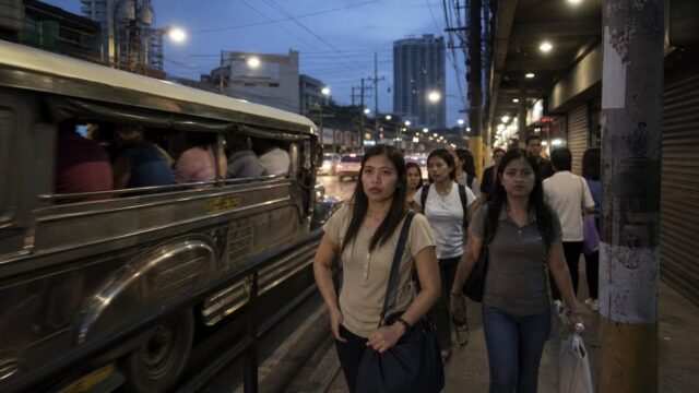 Commuters on a Quezon City street at dusk with a jeepney passing