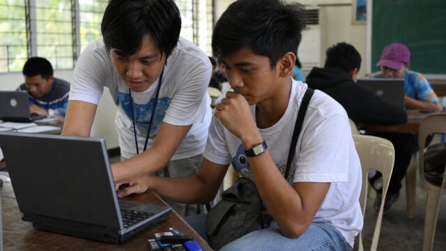 Volunteer helping a student install software on a laptop at a campus install-fest